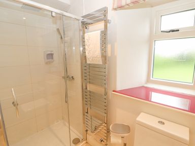 A bathroom with a glass shower enclosure a chrome heated towel rail a toilet and a frosted window at Home Farm House in Penrith