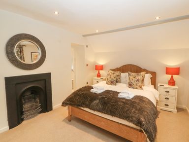 A bedroom with a wooden bed frame and fur blanket two bedside tables with red lamps and a round mirror above a fireplace at Home Farm House in Penrith
