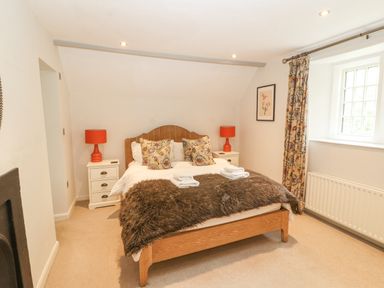 A bedroom with a wooden bed white bedside tables with red lamps floral curtains and a window at Home Farm House in Penrith