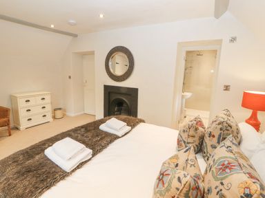 A bedroom with a bed facing a fireplace a chest of drawers a chair and an open door to a bathroom at Home Farm House in Penrith