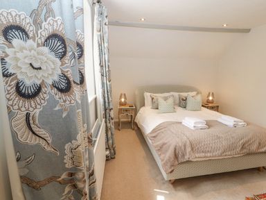 A bedroom with a bed and folded towels on it two bedside tables with lamps and floral curtains at Home Farm House in Penrith