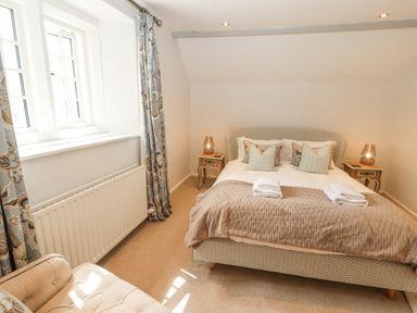 A bedroom with a double bed with pillows and folded towels bedside tables with lamps curtains on the window and an armchair at Home Farm House in Penrith