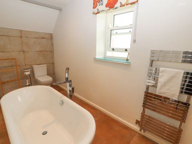 A bathroom with a freestanding bathtub a toilet a heated towel rail and a window at Home Farm House in Penrith
