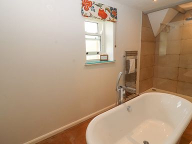 A bathroom with a white bathtub a window with floral valance a towel rack and a shower area at Home Farm House in Penrith