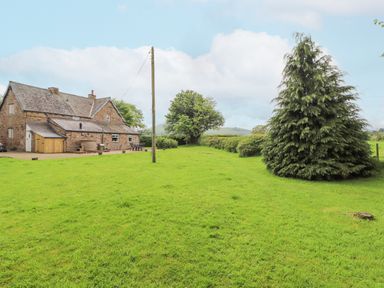 A stone house with a patio area and green lawn with trees and a telephone pole at Home Farm House in Penrith