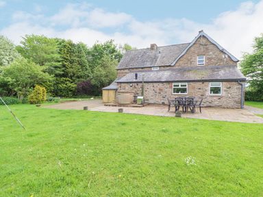 A stone house with a patio and outdoor table and chairs surrounded by grass and trees at Home Farm House in Penrith