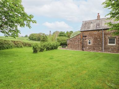 A stone house with a grass lawn and shrubs in a rural area at Home Farm House in Penrith