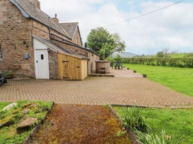 A stone house with a wooden shed attached a hot tub and outdoor seating on a paved patio next to a grassy field at Home Farm House Penrith