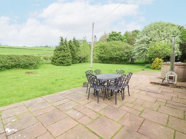 A patio with a round table and six chairs next to a grassy lawn with trees at Home Farm House in Penrith
