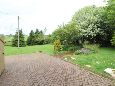 A brick-paved driveway next to a lawn with trees shrubs and flower beds at Home Farm House in Penrith