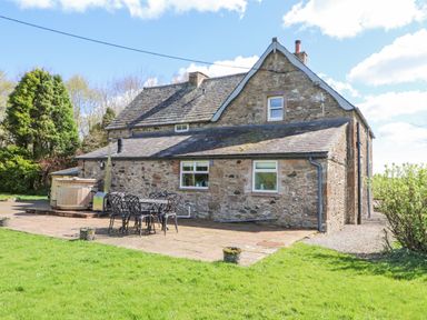 Stone house with patio furniture and a wooden hot tub in a garden at Home Farm House in Penrith