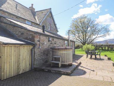Stone house with a wooden hot tub and outdoor table with chairs on a paved patio at Home Farm House in Penrith
