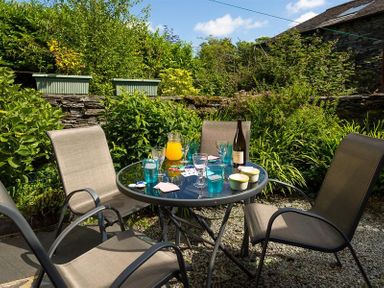 A garden patio with a round glass table and four chairs with drinks and playing cards at Fernleigh Cottage Ambleside