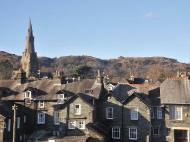 Stone houses with slate roofs and a tall church spire with hills in the background at Fernleigh Cottage in Ambleside