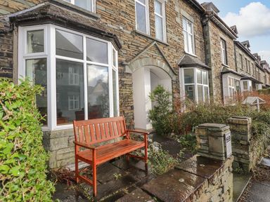 Stone terraced houses with white-framed bay windows wooden bench and small garden at Fernleigh Cottage in Ambleside
