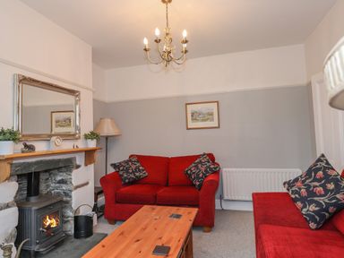 A living room with red sofas a wood stove fireplace and a wooden coffee table at Fernleigh Cottage in Ambleside