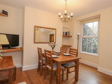 A dining area with a wooden table and four chairs next to a window and wall mirror at Fernleigh Cottage in Ambleside