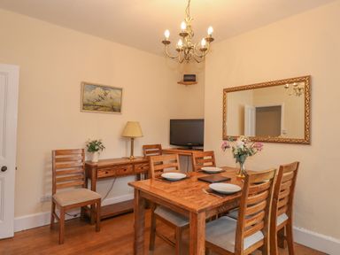 A dining room with a wooden table set with plates and flowers a side table with a lamp a television and a large mirror at Fernleigh Cottage in Ambleside