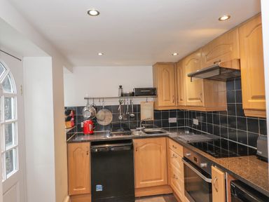 A kitchen with wooden cabinets black appliances and tiled backsplash at Fernleigh Cottage in Ambleside