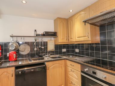 A kitchen with wooden cabinets black tiled backsplash a sink stovetop oven countertop appliances and utensils at Fernleigh Cottage Ambleside