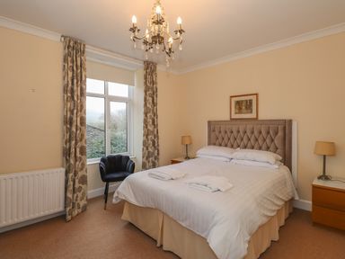 A bedroom with a double bed bedside tables lamps a window with floral curtains and a black chair at Fernleigh Cottage Ambleside