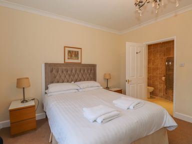 A bedroom with a double bed two bedside tables with lamps and an open door to a bathroom at Fernleigh Cottage in Ambleside