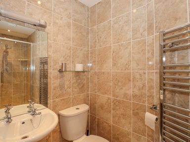 A bathroom with a sink a toilet a glass shelf and a shower at Fernleigh Cottage in Ambleside