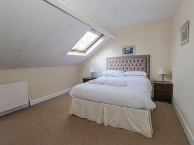A bedroom with a double bed two bedside cabinets with lamps a skylight window and framed pictures on the walls at Fernleigh Cottage in Ambleside