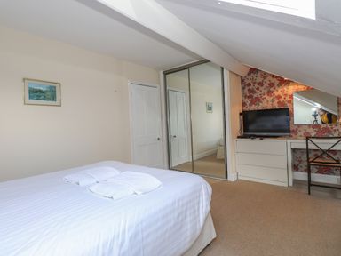 A bedroom with a bed, mirrored wardrobe, TV on a dresser, and a desk with a chair at Fernleigh Cottage in Ambleside