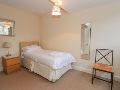 A bedroom with a single bed a bedside table with a lamp a wall mirror and a chair at Fernleigh Cottage in Ambleside