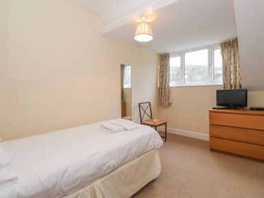 A bedroom with a single bed towels on bed a chair a dresser with a small TV and windows with curtains at Fernleigh Cottage in Ambleside