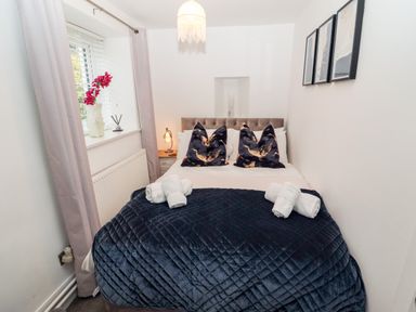 A bedroom with a double bed pillows bedside table with lamp and window with curtains at Riverside Hideaway in Newby Bridge