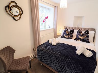 A bedroom with a bed that has dark blue bedding and bird patterned pillows with a brown chair and window at Riverside Hideaway in Newby Bridge