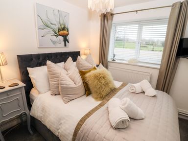 A bedroom with a made bed with pillows and rolled towels by a window with curtains at Riverside Hideaway in Newby Bridge