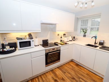 A kitchen with white cabinets a stove oven microwave and sink at Riverside Hideaway in Newby Bridge