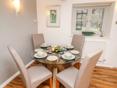 A dining area with a round glass table set for four with plates bowls glasses and chairs at Riverside Hideaway in Newby Bridge