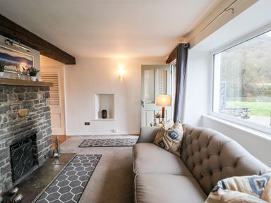 A living room with a stone fireplace a sofa with pillows a table lamp and a large window at Riverside Hideaway in Newby Bridge