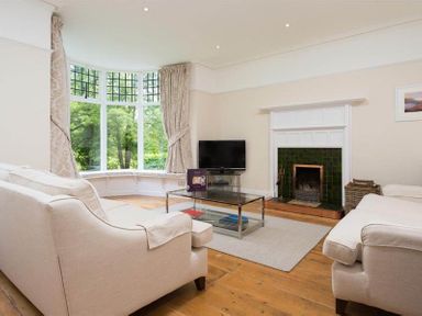 A living room with sofas a fireplace a television and large bay windows at Loughrigg Cottage in Ambleside