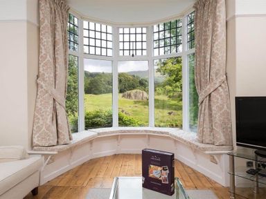 A sitting area with a bay window and curtains overlooking a green landscape at Loughrigg Cottage in Ambleside
