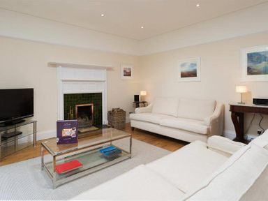 A living room with white sofas a glass coffee table a television and a fireplace at Loughrigg Cottage in Ambleside