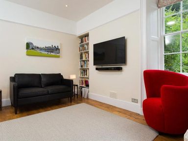 A living room with a black sofa a red armchair a wall-mounted TV and a large window at Loughrigg Cottage in Ambleside