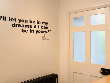 A corner of a room with a white door with glass panels a black radiator and a wall quote by Bob Dylan