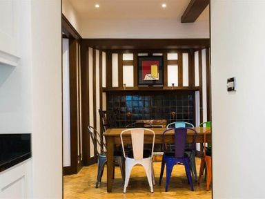 A dining room with a wooden table surrounded by colorful metal chairs and a fireplace with dark tiles at Loughrigg Cottage in Ambleside