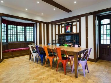 A dining room with a long wooden table and colorful metal chairs near a window seat at Loughrigg Cottage in Ambleside