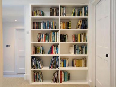 A built in white bookshelf filled with books in a room with white walls and a door at Loughrigg Cottage Ambleside