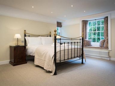 A bedroom with a metal bed frame bedside table with lamp and window seat at Loughrigg Cottage Ambleside