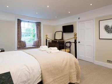 A bedroom with a bed folded towels a window seat with cushions a dresser a wall-mounted TV and a chair at Loughrigg Cottage in Ambleside