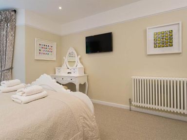 A bedroom with a bed with folded towels a white dressing table a wall-mounted TV and framed pictures at Loughrigg Cottage in Ambleside