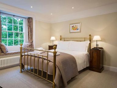 A bedroom with a brass bed frame two bedside tables with lamps and a window seat with cushions at Loughrigg Cottage in Ambleside