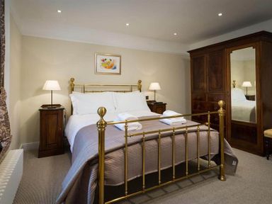A bedroom with a brass bed two bedside tables with lamps and a wooden wardrobe with mirror at Loughrigg Cottage in Ambleside